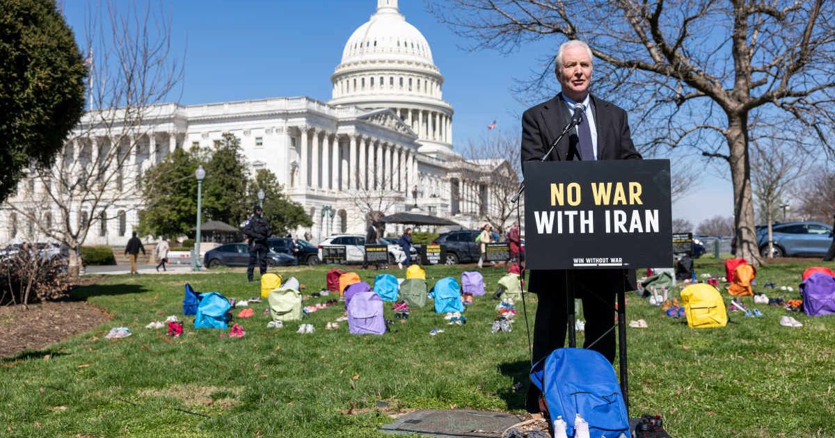 Sen. Chris Van Hollen (D-MD) speaks on Capitol Grounds in front of a memorial of 168 pairs of shoes representing those killed in the U.S. strike on an Iranian school on March 18, 2026, in Washington, DC (Cover Image Source: Getty Images | Photo by Tasos K